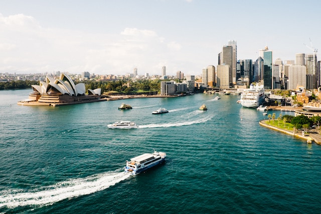 A picturesque view of Sydney's skyline, featuring boats sailing in the water and the renowned Opera House, offering a glimpse into the beauty and attractions of Australia.