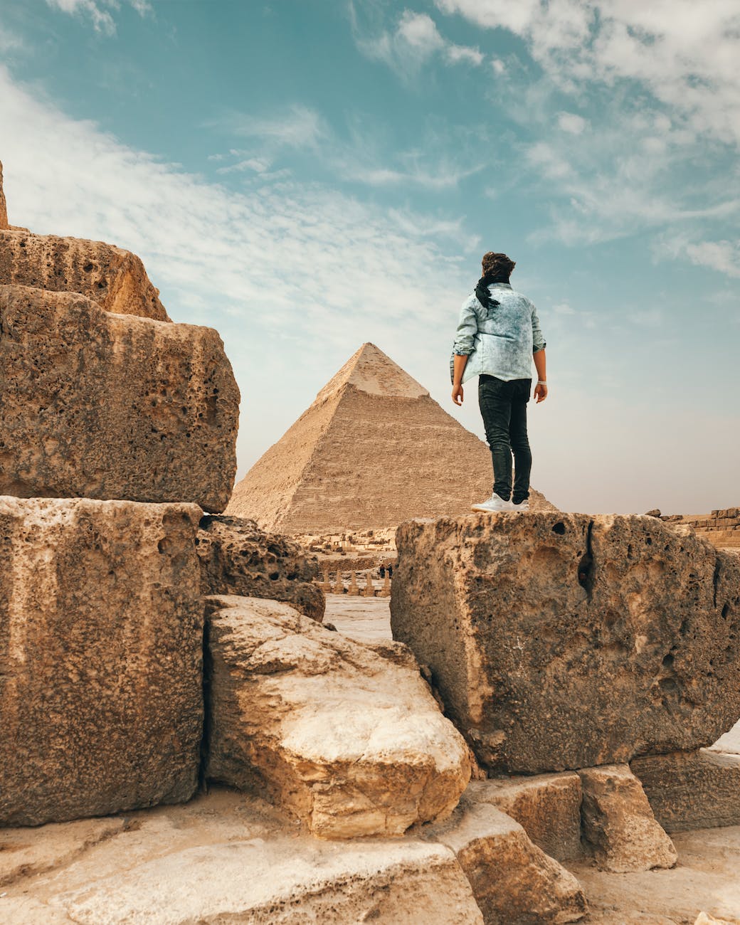 A man triumphantly stands atop a rock, gazing at the majestic pyramids of Giza, Egypt's iconic treasures.