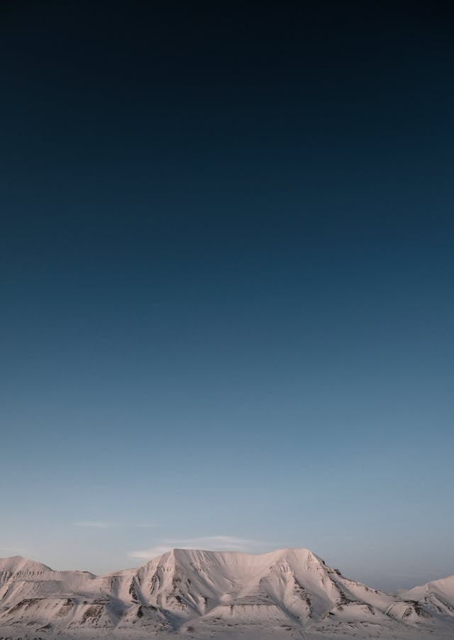 A lone person stands atop a snowy mountain in Svalbard, embracing the serene beauty of the icy landscape. one of the best travel destinations.