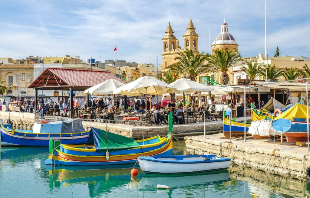 blue and yellow boat on water near brown concrete building during daytime in Malta