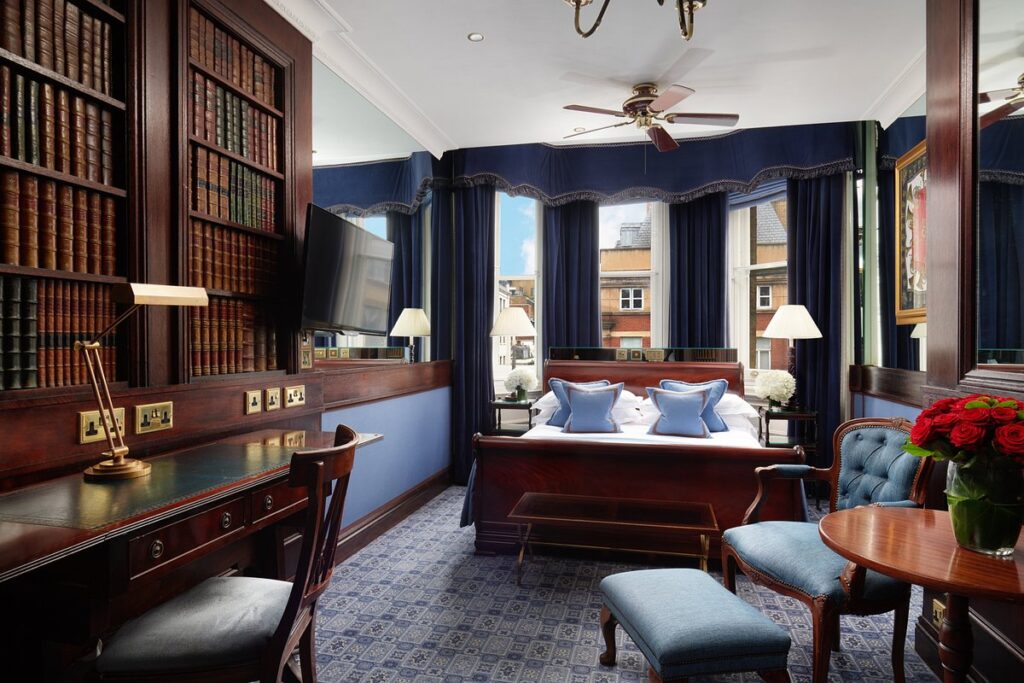 Bedroom with bed, desk, chair, and bookshelves at The Chesterfield Mayfair hotel in London.