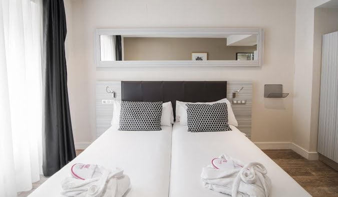 A cozy hotel room at Petit Palace Puerta del Sol in Madrid, featuring two beds and a mirror.