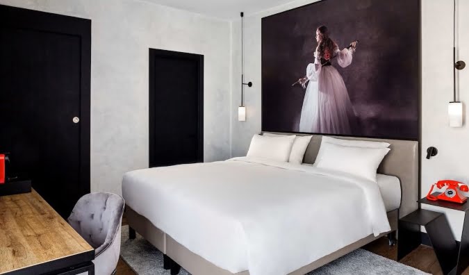 A cozy hotel room in Radisson RED Madrid, featuring a comfortable bed, a functional desk, and a beautiful painting on the wall.