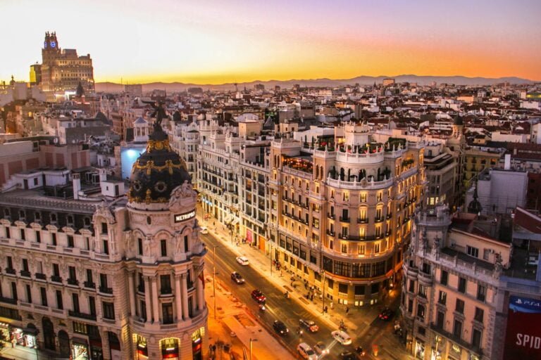 Aerial view of Madrid cityscape with historic buildings and bustling streets under a clear blue sky.