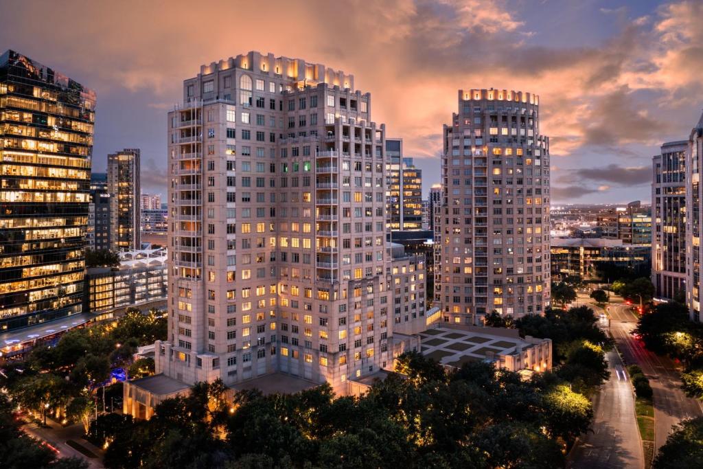 City skyline at dusk with buildings lit up, featuring The Ritz-Carlton, Dallas hotels in the foreground.