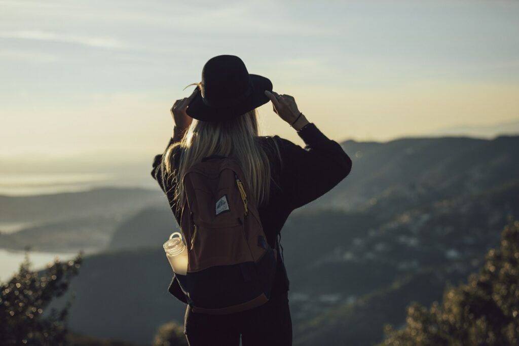 woman in gray hoodie and black pants wearing black hat standing on top of mountain during, budget solo travel destinations.