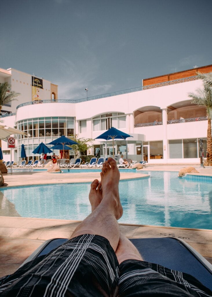 person in black shorts lying on blue and white stripe bed near swimming pool during daytime - Beach Weather in Sharm El Sheikh