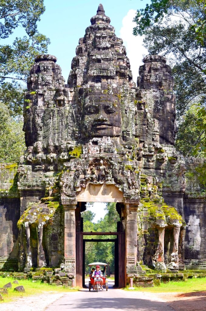 Entrance to Angkor Wat temple in Cambodia, showcasing ancient gray ruins surrounded by lush green trees in daylight.